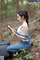 A woman sitting on the ground in the woods writing in a notebook.