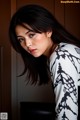 A woman with long black hair leaning against a wall.