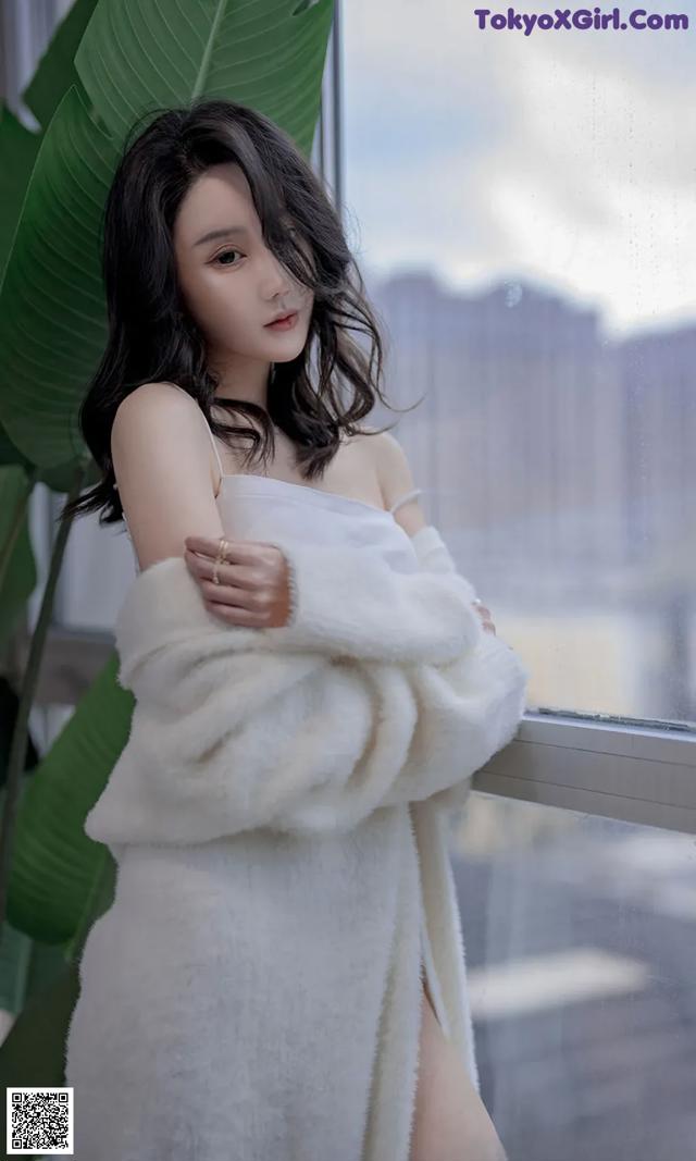 A woman in a white dress standing by a window.