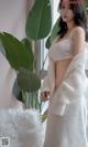 A woman in a white robe standing next to a plant.