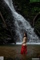 A woman in a red dress standing in front of a waterfall.