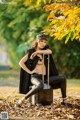 A woman sitting on top of a suitcase in a park.