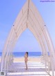 A woman in a white bikini standing in front of a white archway.