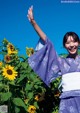 A woman in a blue kimono standing in a field of sunflowers.