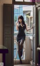 A woman in a black dress standing by a window.