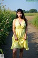 A woman in a yellow dress standing on a dirt road.