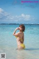 A woman in a yellow bikini standing in the ocean.