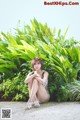 A woman sitting on the ground in front of some plants.