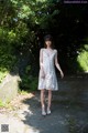 A woman in a white dress standing on a dirt road.