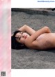 A naked woman laying on the ground in the sand.