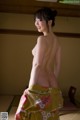 A naked woman in a yellow kimono standing on a tatami mat.