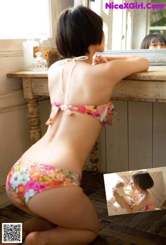 A woman in a bikini sitting on the floor in front of a mirror.