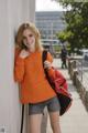 A young woman leaning against a wall with a backpack.