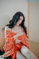 A woman in an orange kimono sitting on a bed.